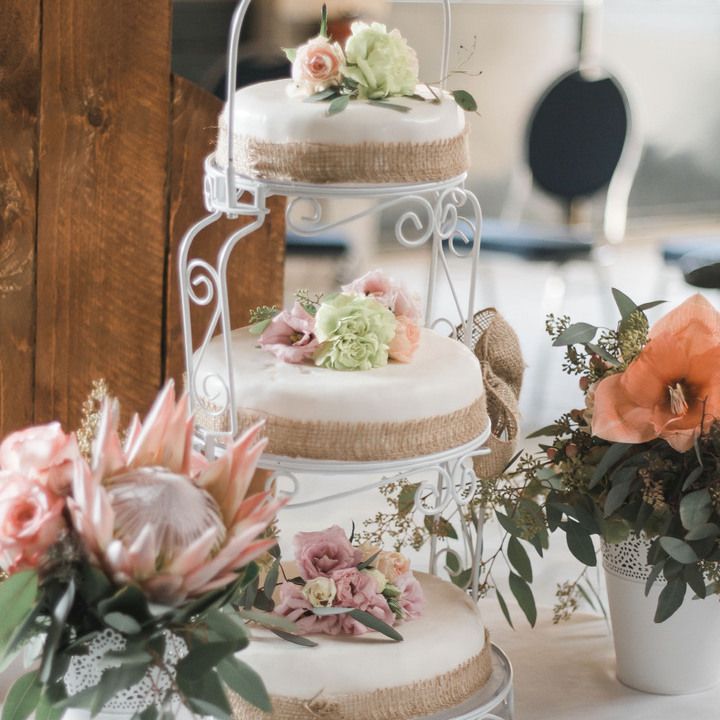 Die Vintagehochzeitstorte ist mit Hanfband verziert und mit blassgrünen Ranunkeln und apricotfarbenen Rosen dekoriert. Sie ist dreistöckig und steht auf einer schmiedeeisernen Etagere.