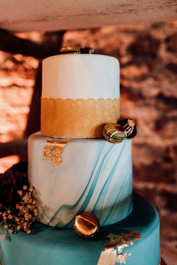 türkismarmorierte dreistöckige Hochzeitstorte mit goldenem Band und Macarons