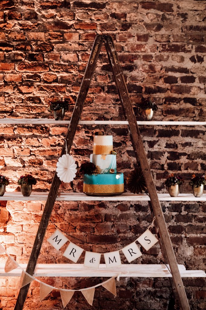 Türkismarmorierte dreistöckige Hochzeitstorte mit goldenem Band und Macarons