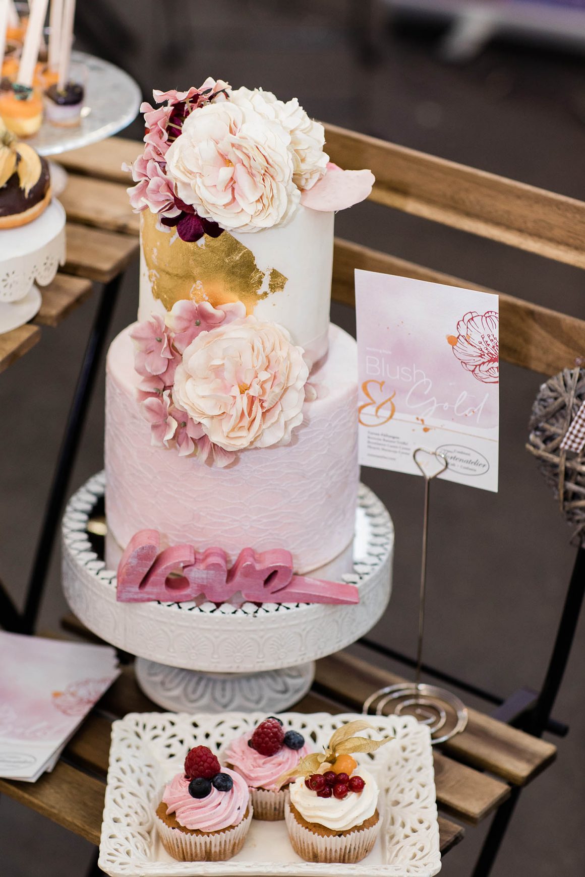 Blushfarbene Hochzeitstorte mit Goldapplikationen und Ranunkeln